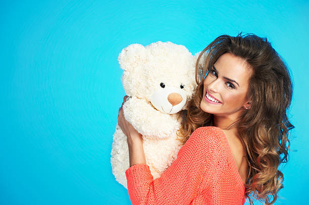 Lovely smiling young woman with big soft teddy bear Happy woman in love in knitted clothes over blue isolated background minion smile stock pictures, royalty-free photos & images