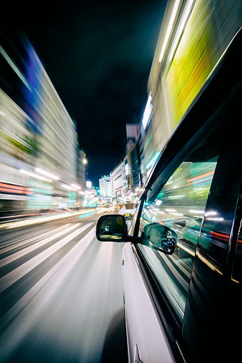 A car drives through the brightly lit Shibuya area of Tokyo, Japan at night. Taken with a remote mounted camera on the exterior of the moving car.