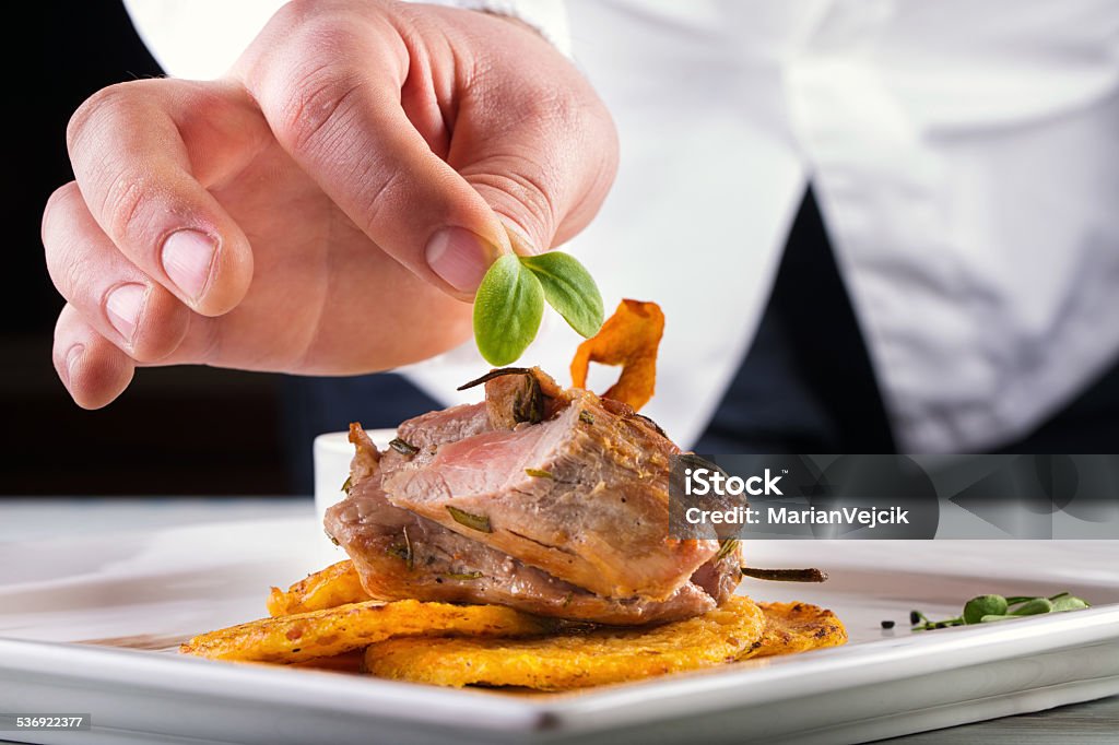 Chef in hotel or restaurant kitchen cooking, only hands. Chef in hotel or restaurant kitchen cooking, only hands. Prepared meat steak with potato or celery pancakes.He is working on the herb decoration. Chef Stock Photo
