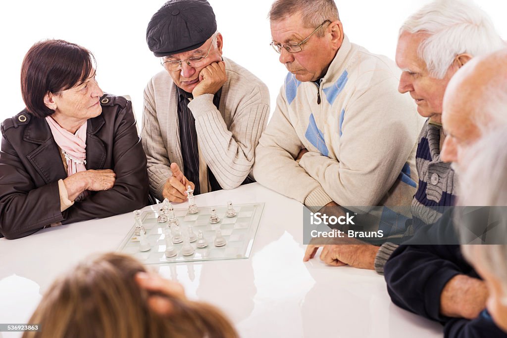 Seniors playing chess. Group of seniors sitting at the table and playing chess in retirement home. Isolated on white. Nursing Home Stock Photo