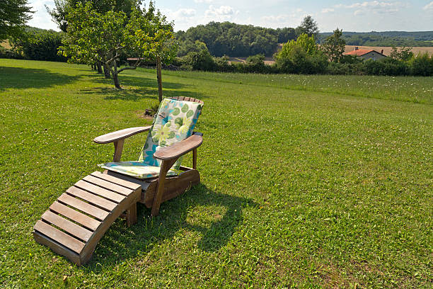 Comfortable wooden recliner chair on a lush green lawn in a rural garden in summer sunshine to relax and unwind