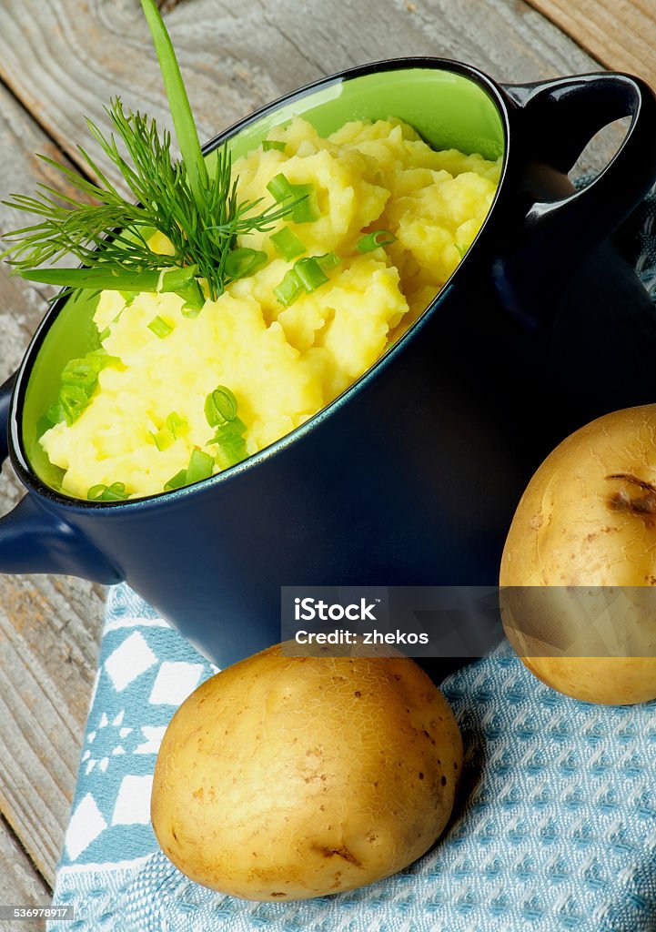 Mashed Potato Creamy Homemade Mashed Potato with Dill and Spring Onion in Casserole on Blue Napkin with Raw Potatoes closeup on Rustic Wooden background 2015 Stock Photo