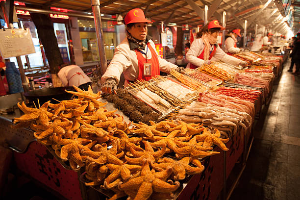 Exotic food market in Beijing, China Beijing, China - January 5, 2012: vendors in the market stalls of the Wangfujing Snack Street, a popular shopping place for tourists and residents alike, where a large variety of common and exotic food is offered day and night. Among other local delicacies this stall offers deep fried starfish. wangfujing stock pictures, royalty-free photos & images