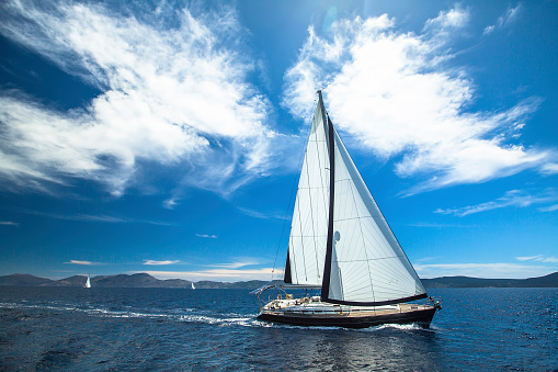 White large Sailboat on the sea, calm water surface with small waves, aerial view from high angle, retraced sail