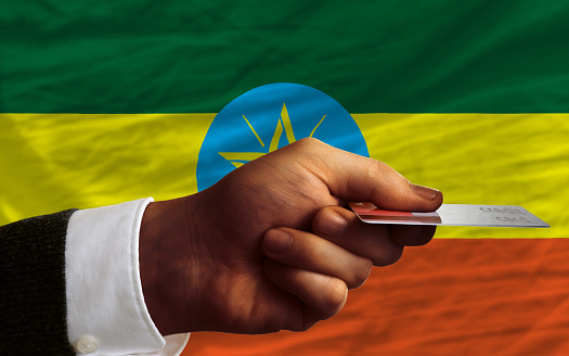 man stretching out credit card to buy goods in front of complete wavy national flag of ethiopia