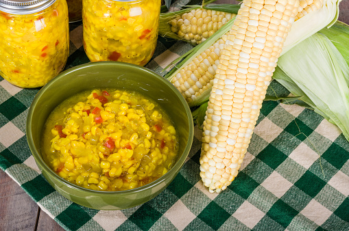 Corn relish in a green bowl with ears of fresh corn