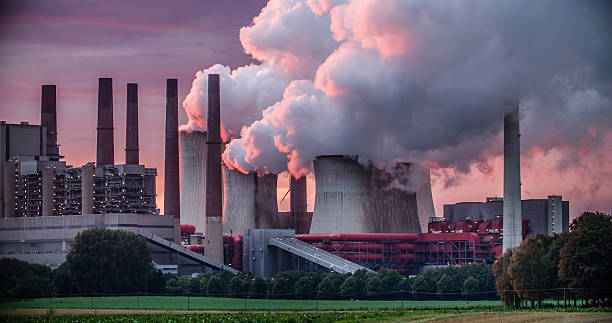 Power Station Chimneys Industry in dramatic red sunset light. Chimneys and cooling tower of a coal fired power station. fossil fuel stock pictures, royalty-free photos & images