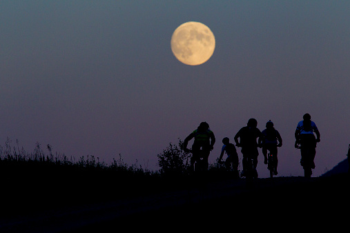 A group of male mountain bike riders compete in a 24 Hour race under a full moon.