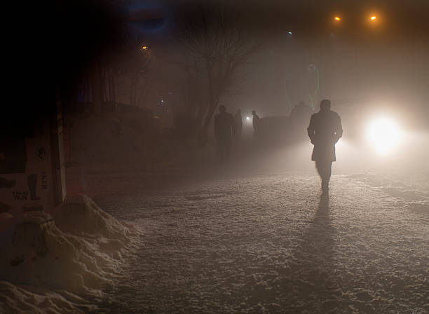 Prague, Czech Republic – January 19, 2024: A lone figure walks down a dimly lit alley at night. The ancient walls, light snowfall, and shadows create a moody, mysterious scene in Prague’s winter streets.