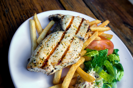Perfectly grilled Tuna or Wahoo steak with salad and fries served on a rustic wooden table