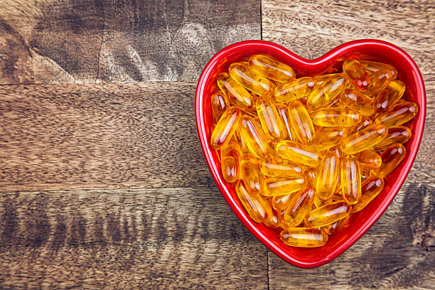 Fish Oil Suppliments Fish oil suppliments in a red heartshaped dish on a wood table cod liver oil fish oil vitamin a pill stock pictures, royalty-free photos & images