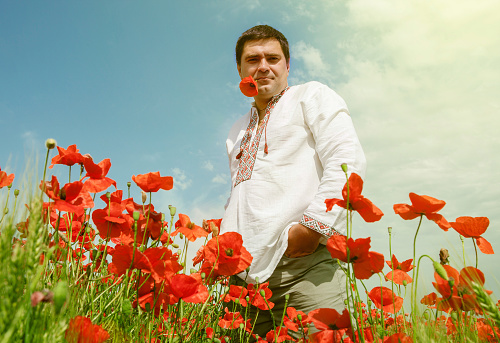 Man in national ukrainian embroidered dress among the poppies flowers