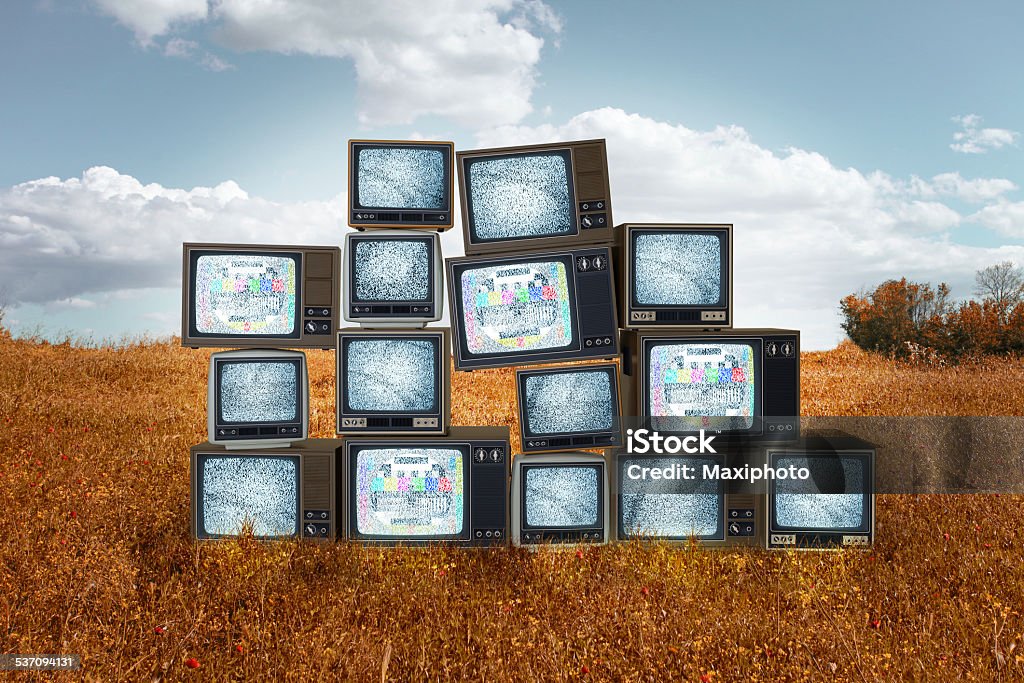 Old televisions stacked in the middle of grass field Stack of old televisions out of context, abandoned outdoor in the middle of a dry grass field, with sky and some clouds in the background.  Television screens show static signal and some test patterns. Computer generated objects on real background. Television Set Stock Photo
