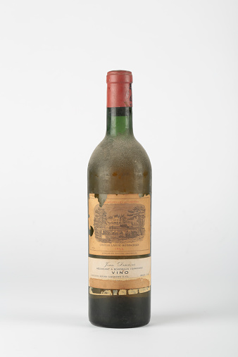 Genoa, Italy – November 4, 2014: Collectable antique bottle of 1964 Chateau Lafite-Rotschild (French red wine), on white background. The bottle is covered with dust and the label is partially torn off.