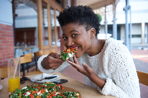 Close up portrait of a young black woman eating vegetarian pizza