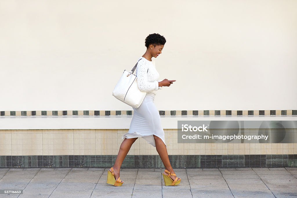 Jeune femme marchant et l'envoi de SMS sur téléphone portable - Photo de Marcher libre de droits