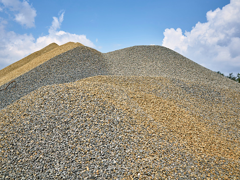 Pile of gravel, crushed stone, outdoors with cloudy blue sky background.