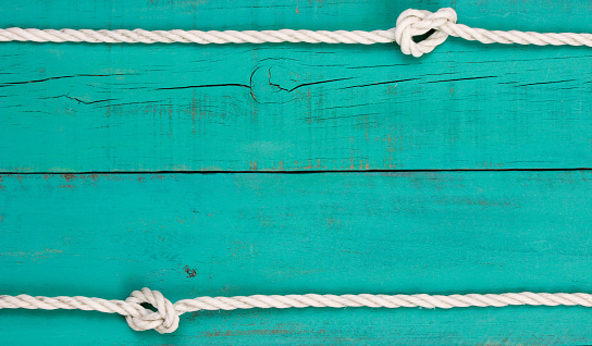 White rope with knots on blank antique teal blue shabby wooden background