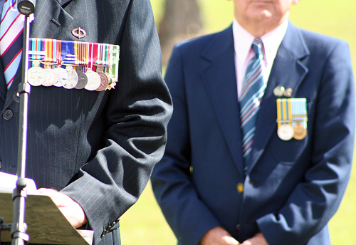 Gold Coast, Australia - April 25, 2010: Two elderly, unidentified, Australian military veterans wearing suits adorned with service medals make a speech at an ANZAC Day memorial service. This image focuses on body language and medals, no faces are visible.
