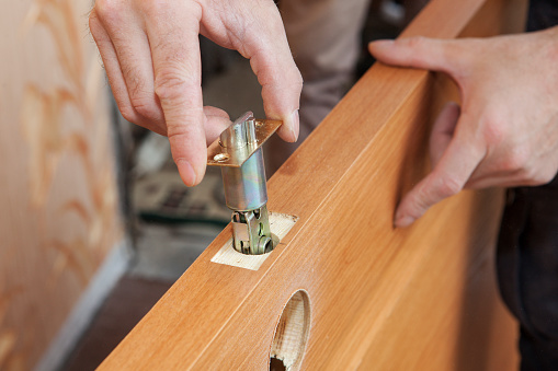 Close-up carpenter hands door lock installation.