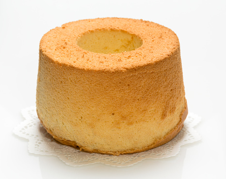 Chiffon cake on a paper doily with characteristic hole in the center from an ungreased tube pan. The cake is made with vegetable oil, eggs, sugar, flour, and flavorings.