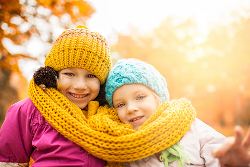 Two happy sisters enjoying outdoors. They are wrapped in scarf and looking at the camera.  