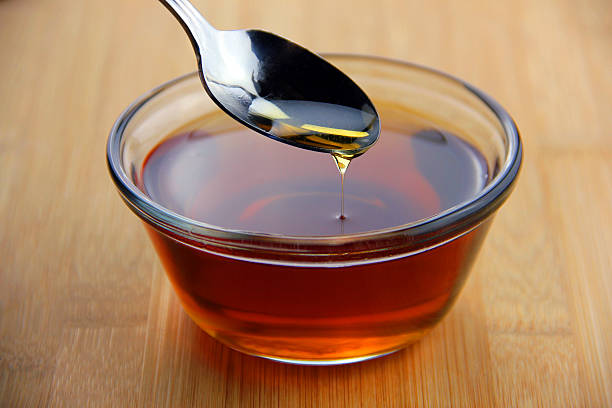 Maple Syrup Maple syrup dripping off of a spoon into a glass bowl set on bamboo wooden surface maple syrup stock pictures, royalty-free photos & images