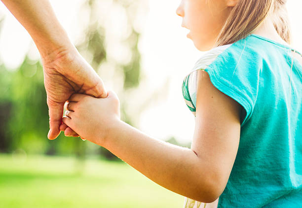 Mother is walking with her daughter in the park and holding hands. A closeup. AdobeRGB profile.