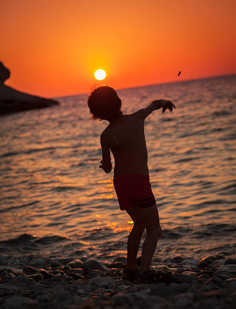 pequeno menino jogando uma pedra em direção ao sol - throwing stone little boys child - fotografias e filmes do acervo