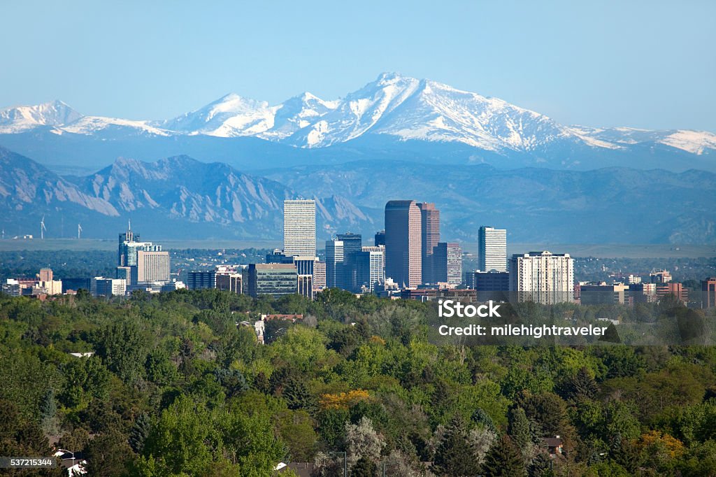 Denver Colorado skyscrapers snowy Longs Peak Rocky Mountains summer Snow covered Longs Peak, part of the Rocky Mountains stands tall in the background with green trees and the Downtown Denver skyscrapers as well as hotels, office buildings and apartment buildings filling the skyline. Denver Stock Photo