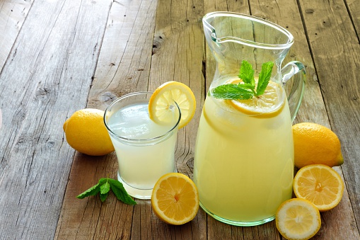 Pitcher of fresh lemonade with filled glass on a rustic wooden background