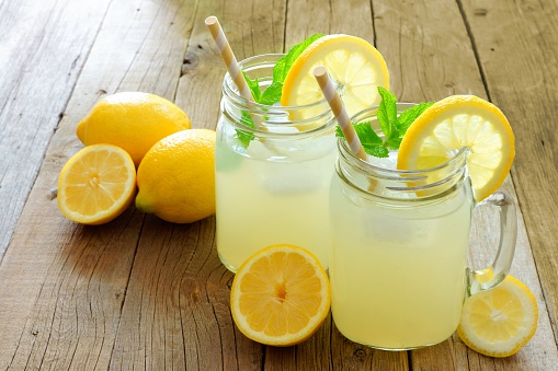 Two mason jar glasses of homemade lemonade on a rustic wooden background