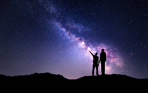 Landscape with Milky Way. Silhouette of a father and son Milky Way with silhouette of a family on the mountain. Father and a son who pointing finger in night starry sky. Night landscape. Beautiful Universe. Space. Travel background with sky full of stars astronomy stock pictures, royalty-free photos & images