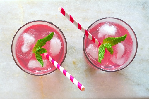 Two glasses of pink lemonade with mint, overhead view on a white marble background
