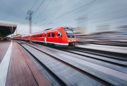 Railway station with modern high speed red passenger train at sunset in Nuremberg, Germany. Railroad with motion blur effect vintage toning. Industrial landscape