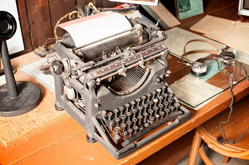 Antique Typewriter and Telephone in a Telegram Office.  Equipment is from the early 20th century.  There is paper in the typewriter.