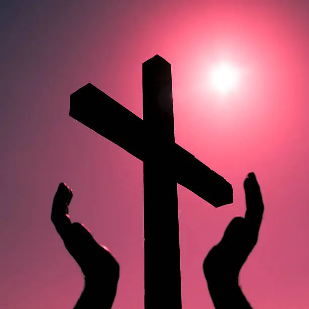 Photo of Silhouette cross and raised hands, bright sun on magenta background