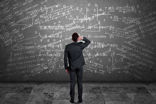 Rear view of pensive businessman scratching his head and looking at mathematical equation on wall