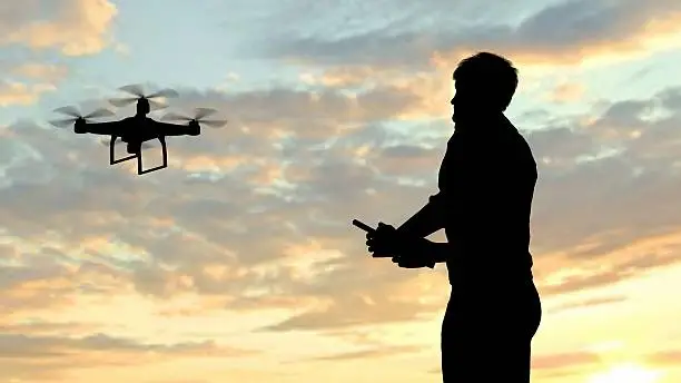 Photo of man operating of flying drone quadrocopter at sunset