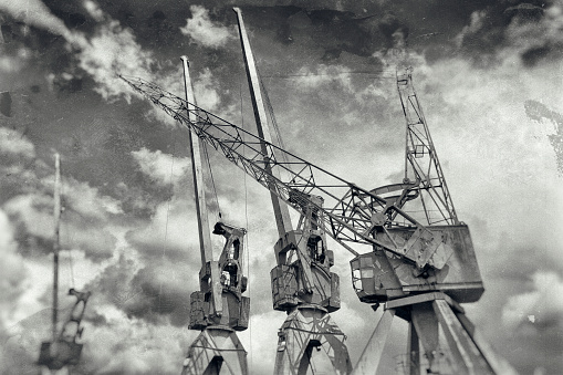 Low angle view of old harbor cranes in a row. Manipulated black and white picture.