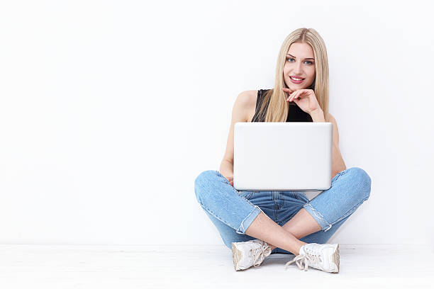 istock Happy young woman sitting on the floor and using laptop 537277578