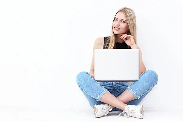 Happy young woman sitting on the floor and using laptop on white background