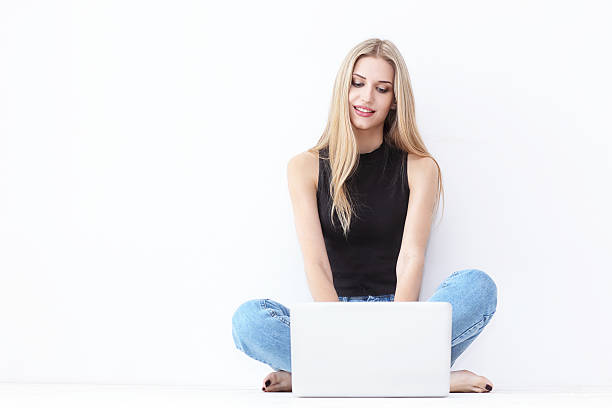 Happy young woman sitting on the floor and using laptop