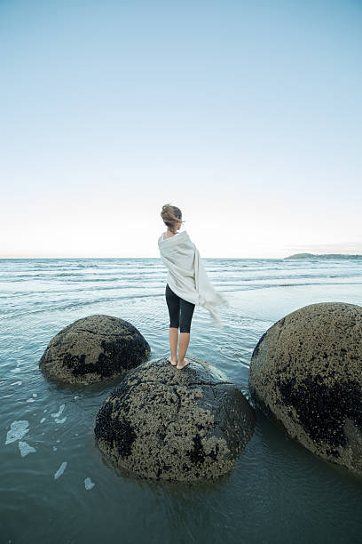 istock Woman wrapped in blanket stands on boulder, looks at view 537286820