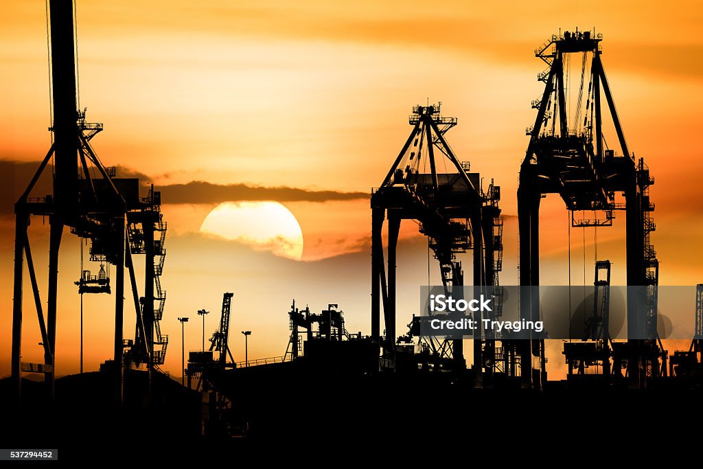 Container Cargo freight ship with working crane bridge in shipyard. Container Cargo freight ship with working crane bridge in shipyard at Silhouette With sunset, Logistic Import Export background concept. Remote Location Stock Photo