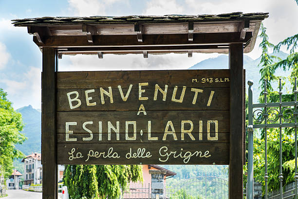 Esino Lario (913 m), Italy, tourist sign Esino Lario, province of Lecco, Italy - May 27, 2016: tourist sign at the entrance of the village. The sign says: "Welcome to Esino Lario the pearl of the Grigne." Esino Lario, venue between 21 to 28 June 2016 of the 12th international Wikimedia conference, is a small mountain village above Lake Como ; Grigne are a mountain massif near the village. In the background, at the bottom, you can see the first houses of Esino Lario wikipedia stock pictures, royalty-free photos & images