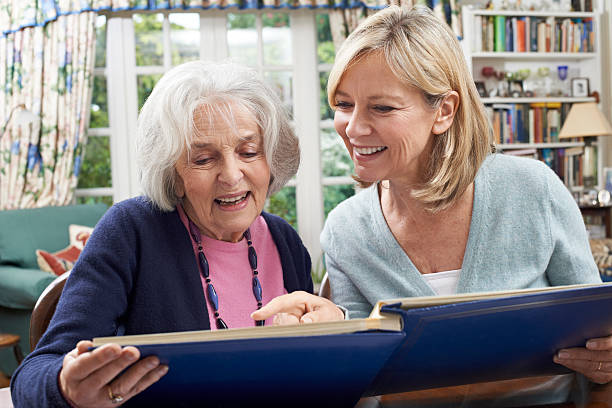 Senior Woman Looks At Photo Album With Mature Female Neighbor Senior Woman Looks At Photo Album With Mature Female Neighbor nostalgia stock pictures, royalty-free photos & images