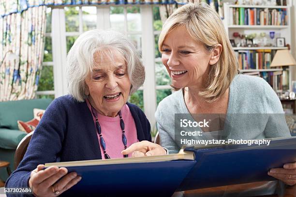 Senior Woman Looks At Photo Album With Mature Female Neighbor Stock Photo - Download Image Now