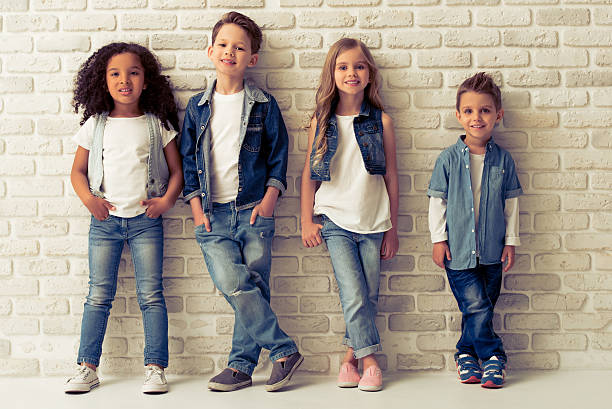 Cute stylish children Full length portrait of cute little kids in stylish jeans clothes looking at camera and smiling, standing against white brick wall children colthes stock pictures, royalty-free photos & images