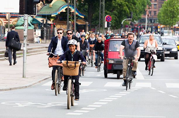 On a Summer day in Madison, WI, bikers wait to cross a busy street on a trail near Lake Monona.